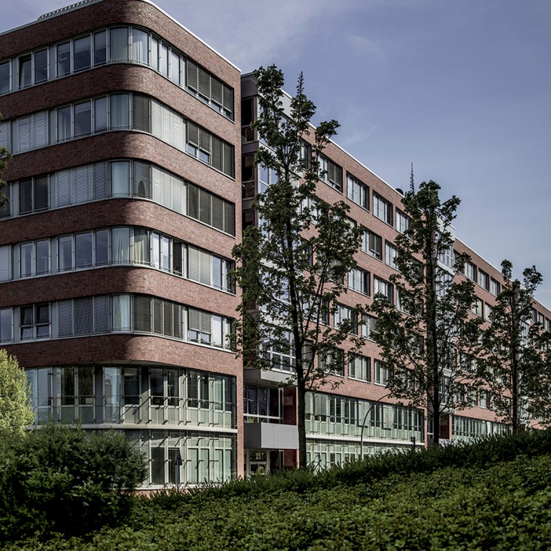 mehrstöckiges Gebäude aus Backstein mit Fensterreihen und Grünfläche im Vordergrund