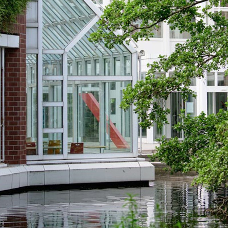 Wintergarten aus Glas an einem Backstein Gebäude und angrenzender Wasserfläche