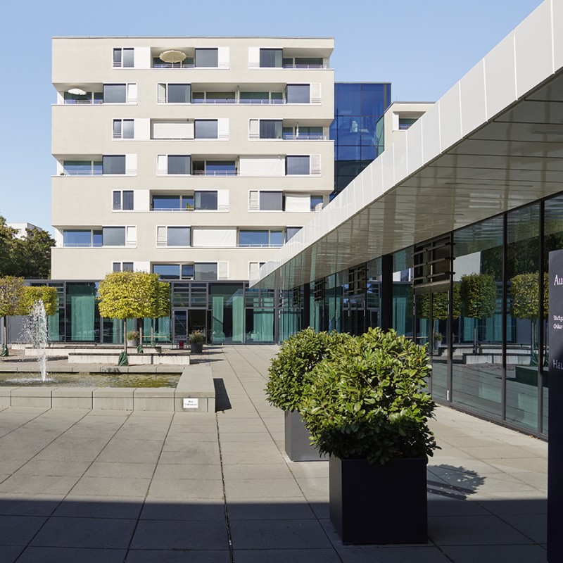 Außenansicht zweier moderner Gebäude mit betonierter Bodenfläche und wenigen Grünpflanzen