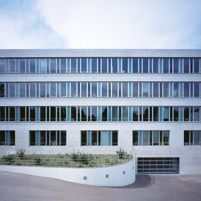 Frontansicht eines mehrstöckigen modernen Gebäudes mit weißer Fassade und Fensterreihen