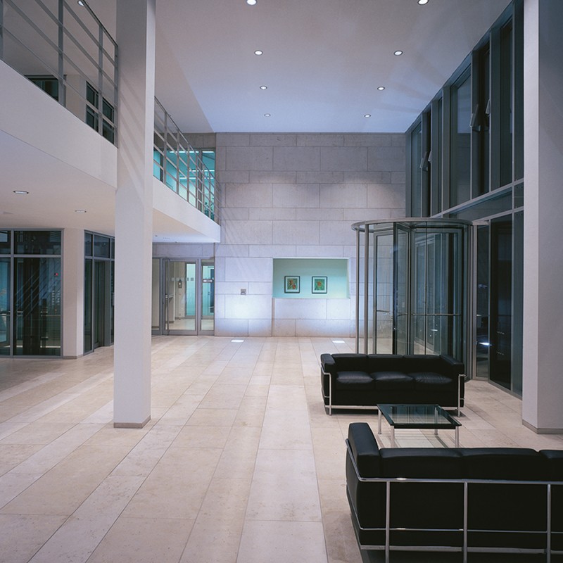 Eingangsbereich eines Gebäudes mit hoher Decke, schlichter moderner Einrichtung und schwarzem Sofa